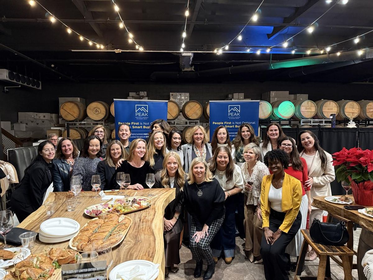 Peak community members around a long table at a winery evening, with Peak banners behind them